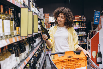 Woman choosing wine bottle in supermarket drinks aisle