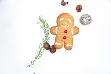 Gingerbread man cookie with shiny red candy buttons surrounded by fresh rosemary, walnuts, dried leaves, and a squiggly sphere seen from above
