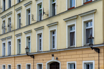 Tenement house in Wrocław with yellow façade, row of white windows, and decorative wrought-iron wall lanterns, typical 19th-century urban architecture.