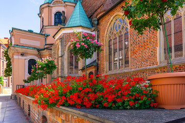 Fototapeta premium Ostrów Tumski in Wrocław, historic church with brick facade, stained glass windows, and red geraniums in planters decorating the entrance.