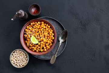 Vegetarian food. Roasted chickpeas with spices and lime in a bowl on black background top view copy space for text