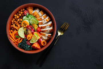 Buddha bowl with baked chicken breast, chickpeas and fresh vegetables on a black background top view copy space for text