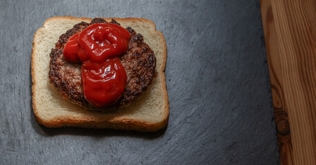 Close-up of a juicy, classic hamburger with generous squeeze of red ketchup. Concepts: Fast food, comfort food, American cuisine, junk food.