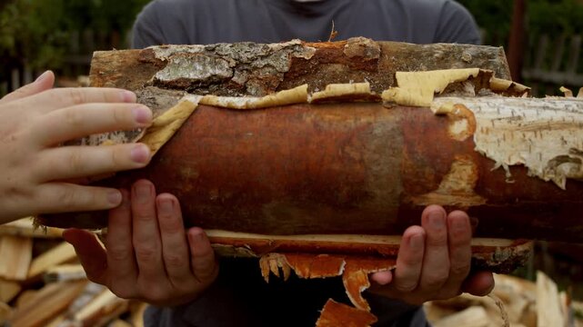 The man picks up the logs in armfuls, stacking them on top of each other and carries them away.