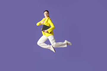 Woman with laptop jumping on purple background