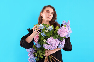 Beautiful woman with bouquet of hortensia flowers on light blue background