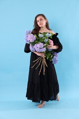 Beautiful woman in dress with bouquet of hortensia flowers on light blue background
