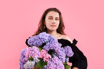 Portrait of smiling woman with hortensia flowers on pink background