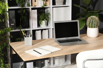 Fototapeta premium Stylish workplace with laptop, stationery and floral decor in office. Biophilic interior design