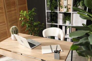 Stylish workplace with laptop, stationery and floral decor in office. Biophilic interior design