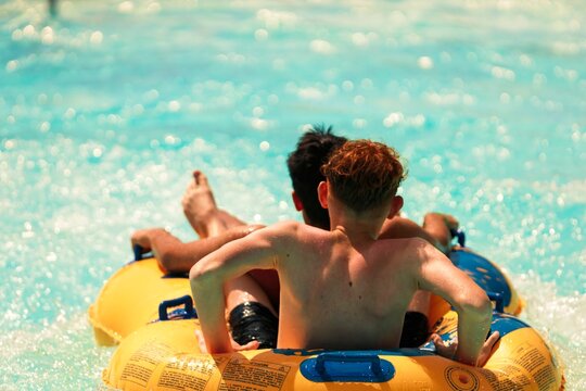 Two figures, viewed from the back, drift along a lazy river within Aquaventure Waterpark. Bright turquoise water creates a refreshing summertime scene in Dubai
