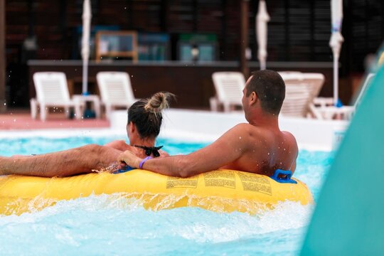 A couple enjoys a relaxing ride together in a wave pool on a bright yellow inflatable tube. They bask in the sun while navigating the gentle waters of the aquatic attraction