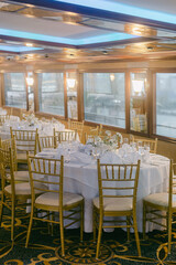 Elegant dining setup in a boat's interior during a calm evening with panoramic windows overlooking the water