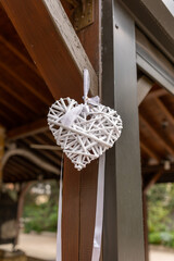 A heart-shaped ornament, intricately woven from white materials, hangs gracefully from a wooden beam. It brings a touch of elegance to the peaceful garden atmosphere, enhancing the rustic charm.