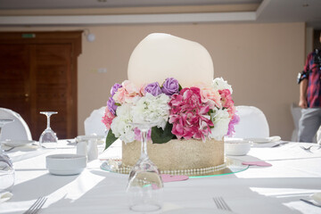 An exquisite floral cake centerpiece adorned with vibrant roses and hydrangeas captivates guests at a luxurious banquet setting. The decorations reflect a joyful, celebratory atmosphere.