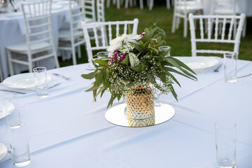 Attendees enjoy a serene outdoor gathering as a pineapple vase filled with fresh flowers serves as a stunning centerpiece on a neatly arranged dining table during sunset.