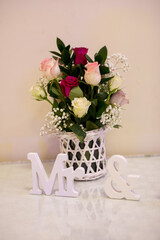 A lovely arrangement of roses in soft hues sits in a decorative basket, alongside charming white letters that spell Mr &. This captures a moment of romance and joy.
