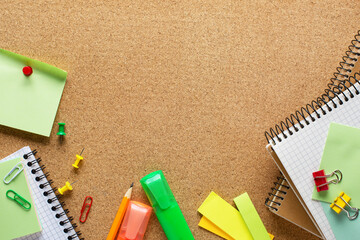 Notepads, markers, pencil, sticky notes, paper sheets, paper clips and binder clips  on cork board  with copy space for text.  Top view of colorful school supplies.