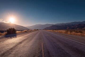 Naklejka premium A long straight road stretches into a mountain range at sunset