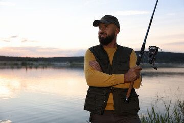 Obraz premium Fisherman with rod fishing near lake at sunset. Space for text
