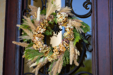Autumn wreath made of dried hydrangea flowers, pampas grass and pine branches hanging on rustic wooden door. Cozy seasonal home decor, countryside atmosphere, vintage style and handmade craft © Volha
