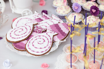 Cookies decorated in purple and pink tones, shaped like cats and swirls, arranged on a party table for a festive celebration.