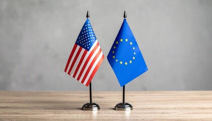 Two miniature flags—United States and European Union—standing side by side on a wooden surface against a plain gray background
