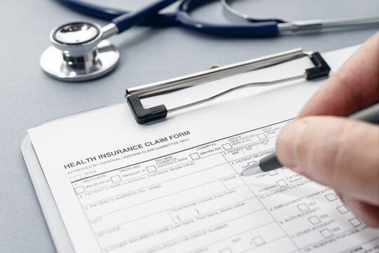 Hand filling on Health Insurance claim form and stethoscope on desk
