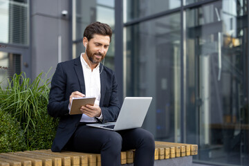 Businessman Taking Notes During a Video Call Outside a Modern Building