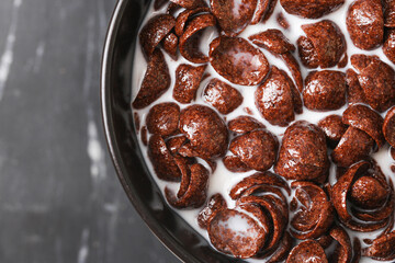 Chocolate cereal with milk in bowl. Sweet crunchy breakfast flakes closeup. Cocoa flavored cornflakes floating in milk. Morning food with dairy. Crispy texture of cereal for healthy meal energy.