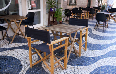 Outdoor cafe scene with wooden tables and chairs on a patterned tiled floor in a vibrant urban setting