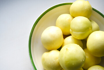 Ripe yellow plum in a green bowl. Juicy fruit on a white background. Ripe plums in drops of water.