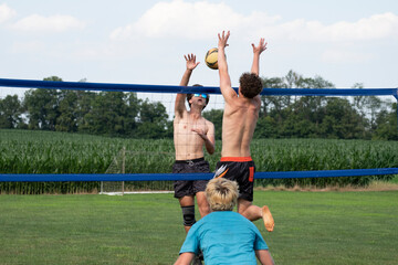 Young volleyball players playing grass doubles next to a corn field