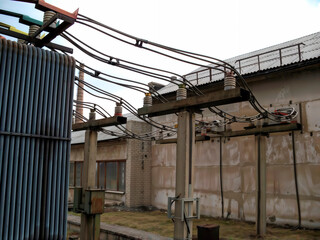 Naklejka premium Input 10 kV to closed switchgear. Heavy electrical cables and busbars connect high voltage equipment next to an industrial building at a power substation.