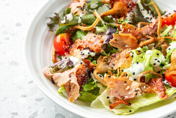 Fresh salad with mixed greens, cherry tomatoes, crispy bacon, fried mushrooms, creamy dressing, and sesame seeds in a white bowl, close-up.