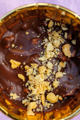 Close up of creamy chocolate dessert topped with crushed nuts in golden wrapper on purple background