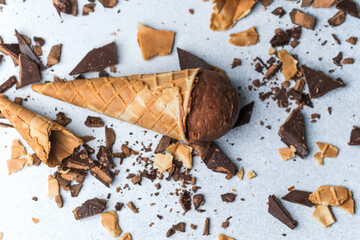 Waffle cone filled with chocolate ice cream lying on light surface with chocolate chunks and waffle crumbs