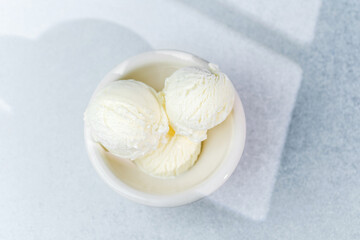 Vanilla ice cream scoops in white bowl on light surface in daylight