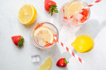 Strawberry lemon infused water in clear glasses with ice cubes and striped straws served on bright table