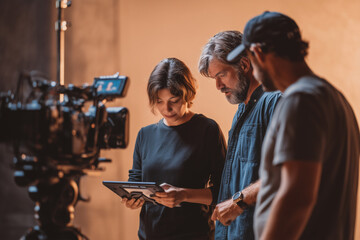 Young woman collaborating with middle aged man and Young man using digital tablet on film set, professional crew discussing project