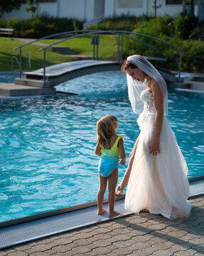 Braut im Brautkleid spricht am Poolrand mit ihrer Tocher