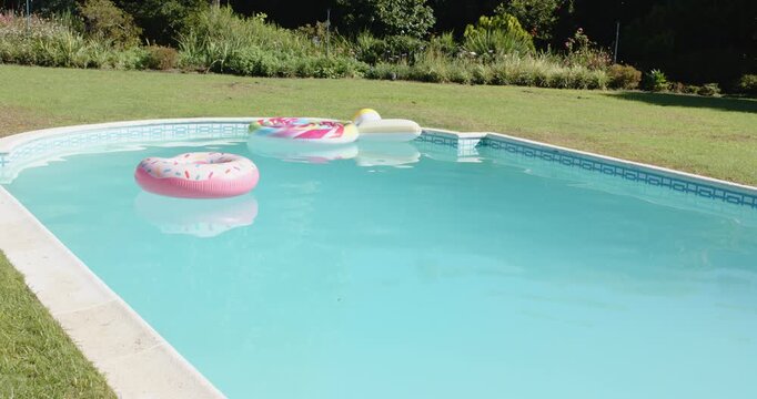 Pink doughnut, lollipop ring and popsicle floats drifting on light-blue garden pool with stone edge