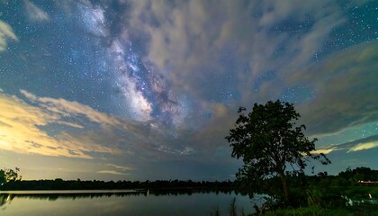 A tranquil lake scene under a vast night sky, featuring the Milky Way and a solitary tree.