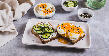 Open sandwiches with ricotta, cucumber and soft-boiled egg on a plate on a table web banner