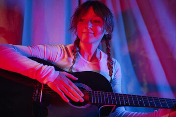 Young woman with two braids playing acoustic guitar, surrounded by vibrant blue and red neon lights, creating an artistic and lively atmosphere filled with musical passion