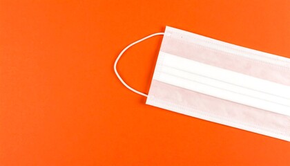 A white protective face mask lies on a vibrant orange surface, highlighting the importance of personal safety.