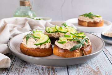 Appetizing sandwiches with cod liver pate, cucumber and arugula on a plate on the table