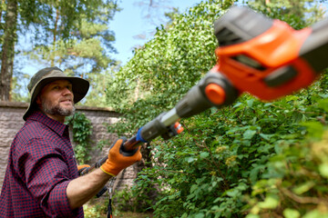 Man trimming bushes using an orange gardening tool in a green outdoor garden