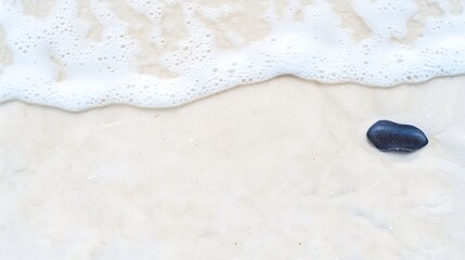 Obraz premium A single dark stone rests on wet sand as a gentle wave washes ashore