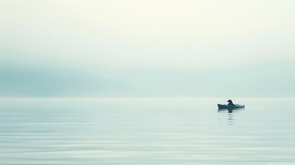 Naklejka premium A lone figure in a small boat on a vast, misty body of water